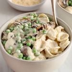 Tahini pasta topped with roasted mushrooms and green peas. There is a fork in the bowl.