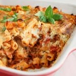 Close up on a vegan baked ziti dish that's still in its baking dish with a portion that was remove to show its interior texture. You can see pockets of creamy cashew cream mixed in with the marinara sauce.