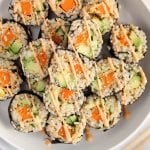 Close up on a few sweet potato sushi rolls pilled on a large white plate. The vegan maki are topped with sesame seeds and a drizzle of spicy mayo sauce.