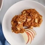 Over head view on a close up on 2 sweet potato cookies on a white plate with a few slices of apple on the side. There is a cup of coffee and more cookie on the side of the plate on the table.