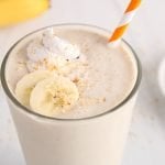 Close up on a glass that's filled with a homemade coconut milkshake. The glass is topped with coconut whipped cream, sliced bananas and toasted shredded coconut.