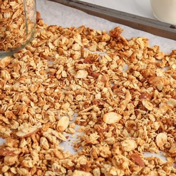 Showing is a baking sheet containing a homemade vanilla almond granola with a jar containing some of the granola for storage.