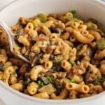 Front angle view on a bowl filled with a vegan hamburger helper while a fork is taking some. There is a close up on the noodles on the fork to show the creamy rich texture.