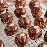 Front angle view on a circular shaped cooling rack that's topped with a few ball shape chocolate peanut butter rice krispie treats. The treats are topped with melted chocolate, sea salt and a peanut.