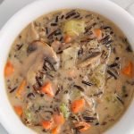Close up on an overhead view on a bowl of vegan wild mushroom soup. There is a spoon on the side of the bowl as well as black pepper topping the soup.