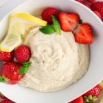 Overhead on a close up on a bowl filled with a vegan mascarpone cheese. There are strawberries and raspberries into the bowl as well as lemon slices around the bowl.