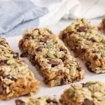 Front angle view on a few vegan nut-free granola bars filled with chocolate chips and cranberries that are placed on a wooden board covered with parchment paper.