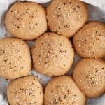 Overhead view on a cast iron pan that was covered with some parchment paper and contains 8 healthy vegan buns that were just baked. You can see there everything bagel seasoning covering their surface as well.