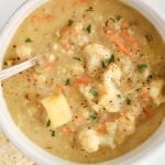 Overhead close up on a chunky vegan leek and potato soup. There is a spoon in the bowl as well as a garnish of fresh parsley.
