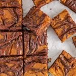 Overhead view on a few squares of a vegan pumpkin swirl brownies placed on a parchment paper. There is one of the square that's lifted to show the layers.