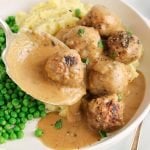 Close up on a large spoon that's adding a vegan TVP meatballs soaked in a gravy over mashed potatoes.