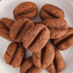 Close up on a few eggless coffee bean cookies on top of each other with the focus on the top cookie. The cookies are shaped like coffee beans.
