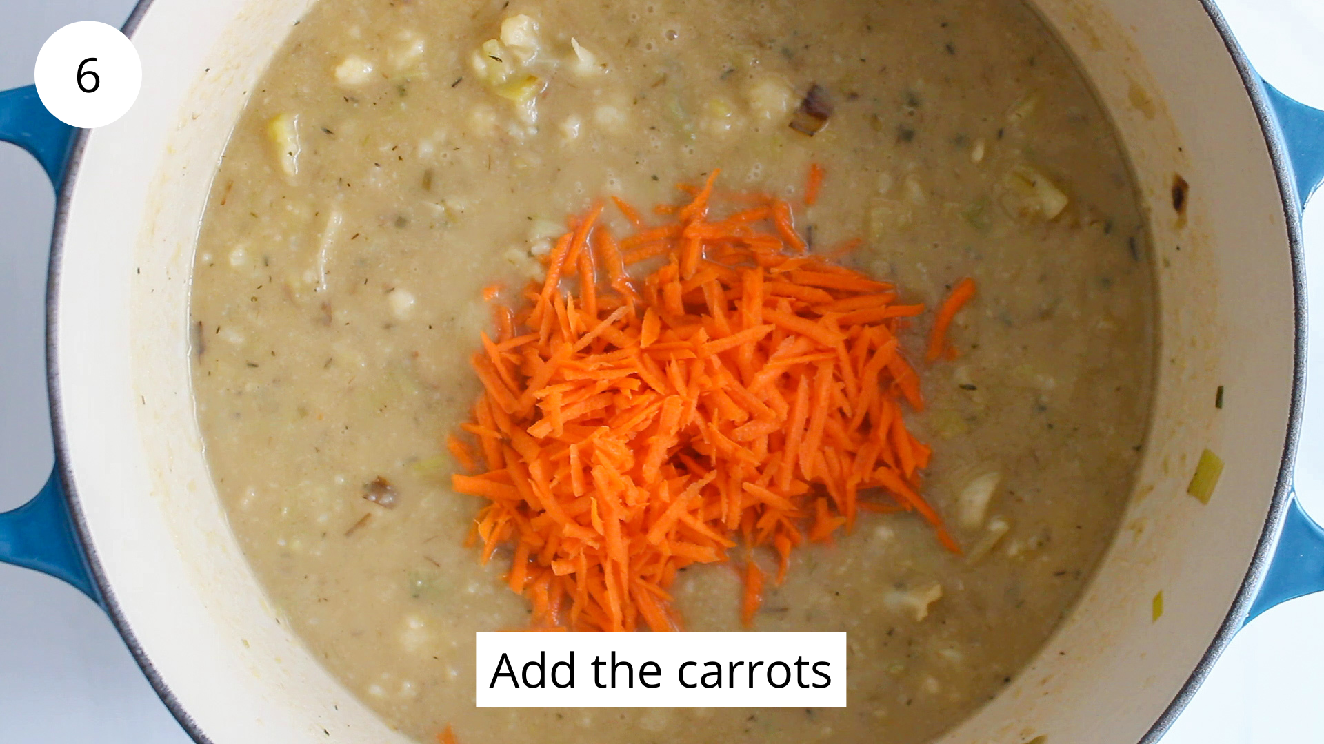 In process picture: there is a large pot filled with a creamy soup topped with shredded carrots.