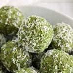 Close up on a no-bake coconut ball placed into a bowl with more balls.