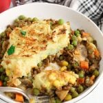 Close up on a plate containing a vegan mushroom and lentil shepherd's pie with a fork that's taking a bite.