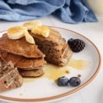 Showing are a few homemade buckwheat banana pancakes on a plate with a bite taken off to show the texture.