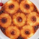 Close up on a circular pineapple and cherry vegan upside down cake with more cherries on the side.