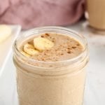 Close up on the top portion of a glass of chai smoothie that's garnished with sliced bananas and more spices.