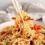There are some chopsticks taken some of the vegan spicy garlic noodles from a bowl.