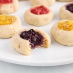 Close up on a vegan blueberry thumbprint cookies made with almond and oat flour. There is a bite taken off the cookie to show the middle texture.