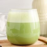 Close up on a see-through mug containing a bright green oat milk vanilla matcha latte.