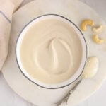 Close up on a bowl of vegan vanilla frosting with a few raw cashews on the side.