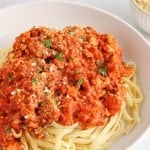 Front angle view on a bowl filled with linguini and topped with a vegan bolognese made with tofu and a marinara sauce.
