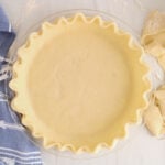 Overhead view on a coconut oil vegan pie crust still empty and uncooked with a blue hand towel on the side.