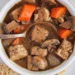 Overhead view on a bowl filled with a vegan tempeh beef stew with a spoon inside and chunks of carrots.