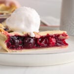 Side view on a slice of vegan cherry pie topped with a scoop of vegan ice cream.
