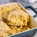 Close up on a spoon that's taking a portion of a vegan baked cauliflower mac and cheese out of a dish. You can see clearly the creamy filling and the crumbly topping.