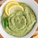 Close up on a small white bowl filled with a vegan walnut pesto topped with slices of lemon and fresh basil leaves.