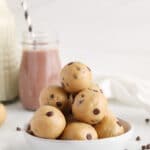 Front view on a few healthy edible cookie dough bites (no brown sugar) place on a plate with some vegan chocolate milk in the background.