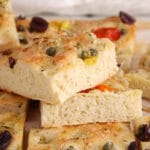 Close up on a few pieces of vegan tomato focaccia bread pilled over each other to show how thick there are and their middle texture.