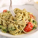 There is a fork taking a bite from a bowl of vegan avocado pasta.