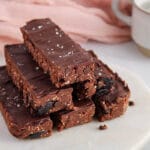 There are a few chocolate oatmeal no bake bars piled over each other and placed on a wooden board.