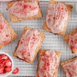 Overhead view on a few vegan strawberry pop tarts placed on a cooling rack with a side of extra frosting and freeze dried strawberries.