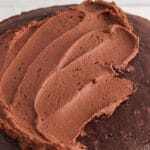 Showing is the top of a chocolate cake that's half covered with a healthy vegan dark chocolate frosting.