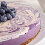 Front angle view on a vegan blueberry cheesecake topped with more blueberries. You can see the date-nut crust and the blueberry vanilla swirl.