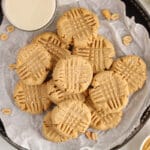 Overhead view on a dark plate filled with 3-ingredient almond flour peanut butter cookies with a glass of milk on the side.