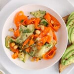 Overhead view on large plate containing a bowl of Asian carrot and cucumber salad with a side of avocado toasts.