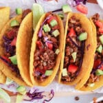 Overhead view on a few taco shells filled with a vegan lentil walnut taco meat, fresh tomatoes, avocado and red onions.