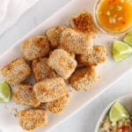 Overhead view on a few oven-baked crispy crusted coconut tofu bites on a plate with a side of orange sauce.