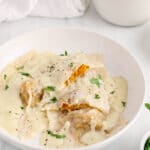 Showing are a few vegan ravioli made with butternut squash and topped with a vegan bechamel sauce. The top ravioli is sliced in half to show the middle squash filling.