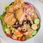 Close up view on a baked falafel buddha bowl filled with produce and drizzled with a homemade spicy tahini sauce and sesame seeds over.
