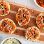 Overhead view on a few halved bagels topped with vegan cream cheese and garnished with a vegan carrot lox, red onion and capers.