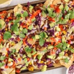 Overhead view on a large baking sheet filled with vegan nachos loaded with lentils, vegan white queso and fresh produce.