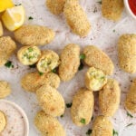 Overhead view on a few vegan potato croquettes on a parchment paper with 2 bowls filled with ketchup and a creamy yogurt sauce.