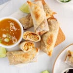 Overhead view on a plate containing a few vegan tofu egg roll with one sliced in half to show the middle texture. There is a side orange sauce.