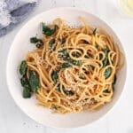 Overhead view on a kale noodle dish sprinkled with sesame seeds and black pepper.